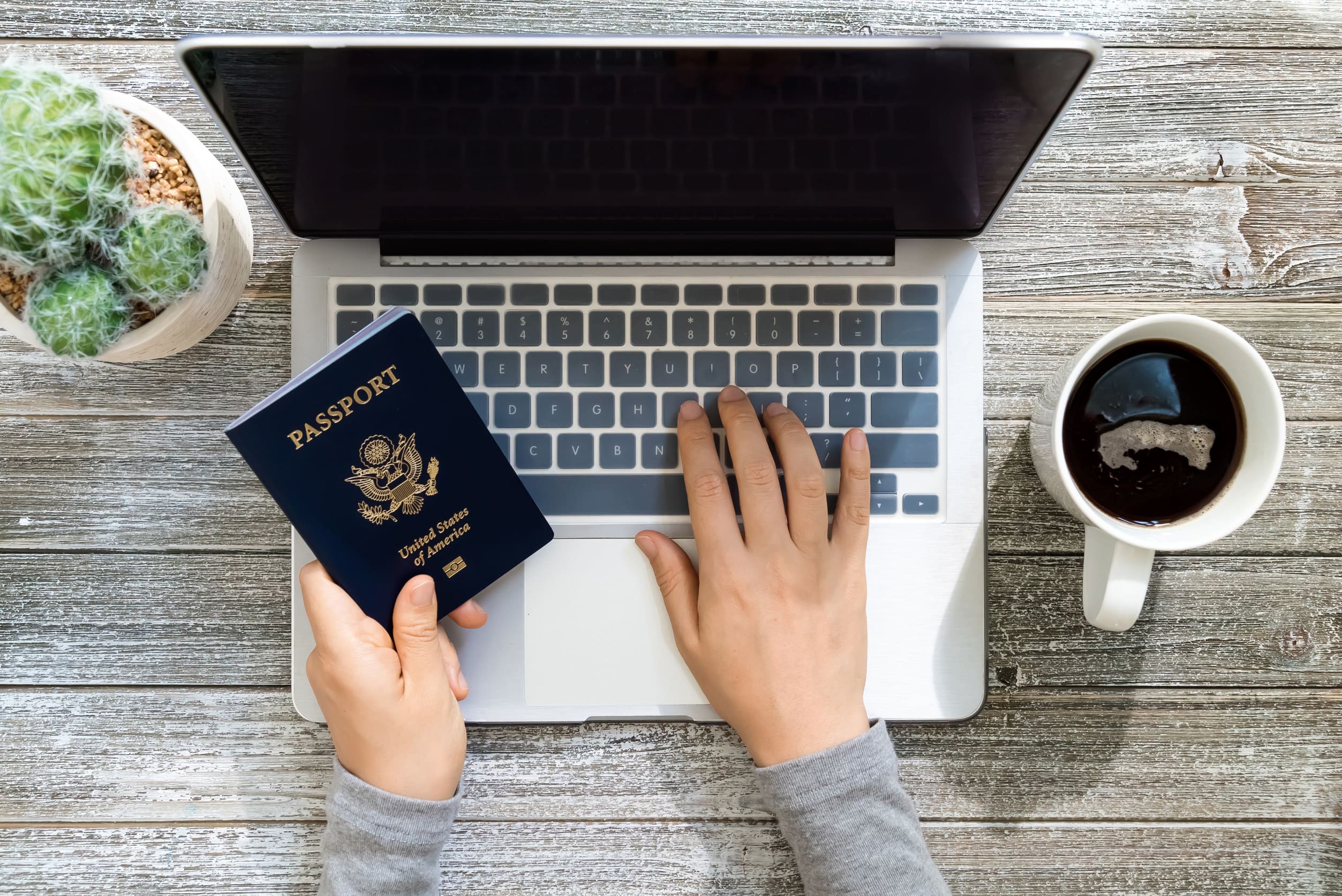 Person Holding An American Passport While Using A Laptop Person Holding An American Passport While Using A Laptop